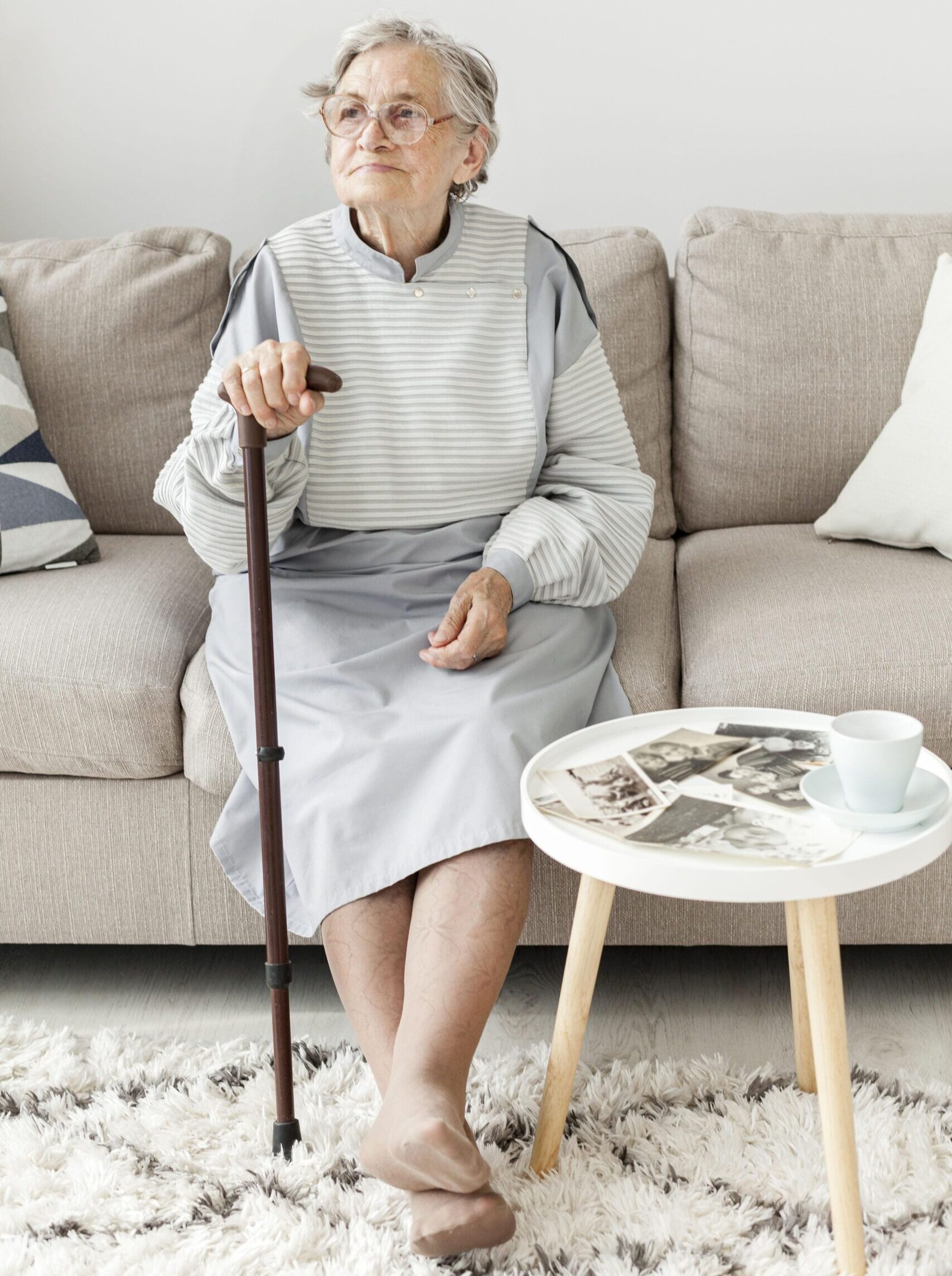 Eine ältere Dame sitzt mit ihrem Gehstock auf einem Sofa.